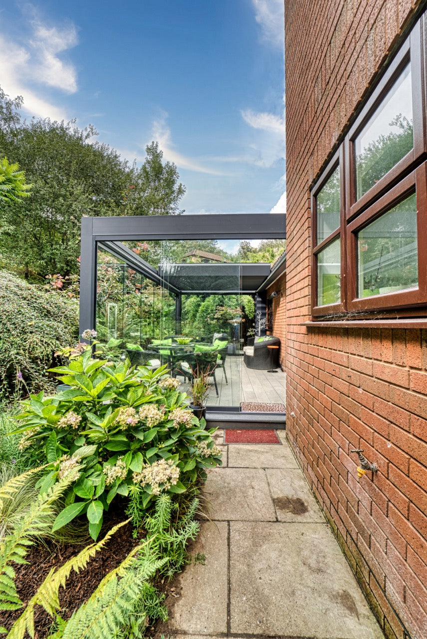 Aperto pergola in anthracite from garden at mid-morning, panels partially angled